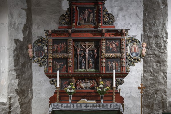 Richly decorated wooden altar in front of a stone wall, adorned with images of saints, candles and