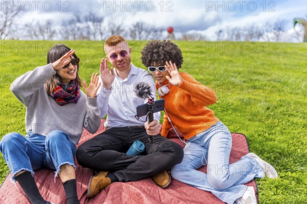 Three content creators waving cheerfully at the camera while filming a video blog outdoors in a