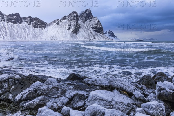 Iced rocks on the beach of Stokkness, behind them the snowy rocky slopes of Vestrahorn, near Höfn,