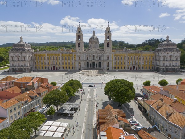 Historic baroque-style palace with yellow façade and two towers, under blue sky and large square,