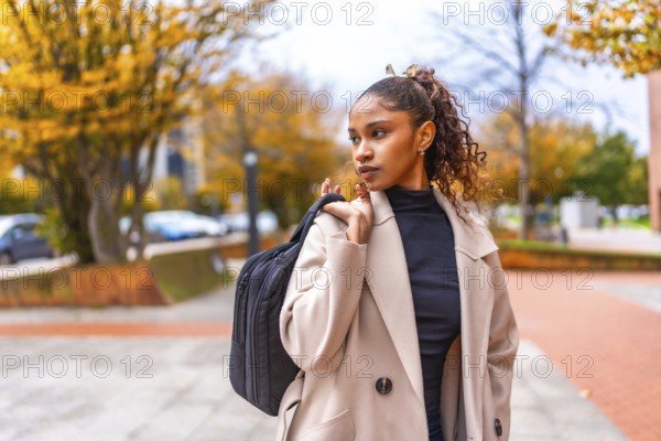 Elegant african american young businesswoman wearing trench coat carrying hand bag in the city in