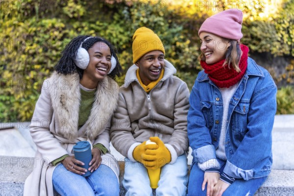 Three cheerful young multi ethnic friends sitting outdoors in the city on a cold winter day,