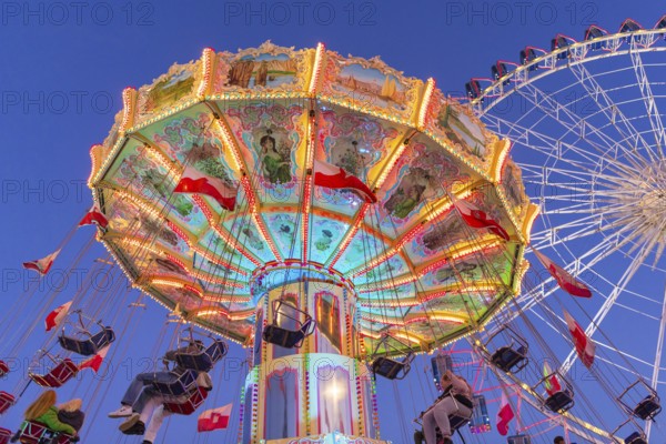 Illuminated carousel and Ferris wheel at night in a lively amusement park, funfair, wave flight,