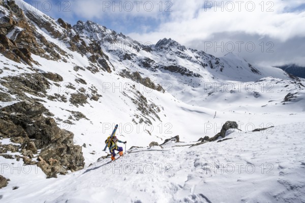 Mountaineer with skis climbing up a steep snow slope to the fork Porta d'Es-cha, ski tour Bündner