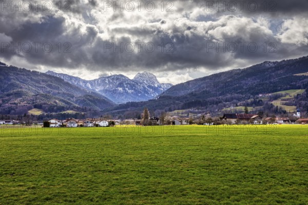 Dramatic Alpine landscape with green meadow in the foreground and cloudy sky over a village, Bad