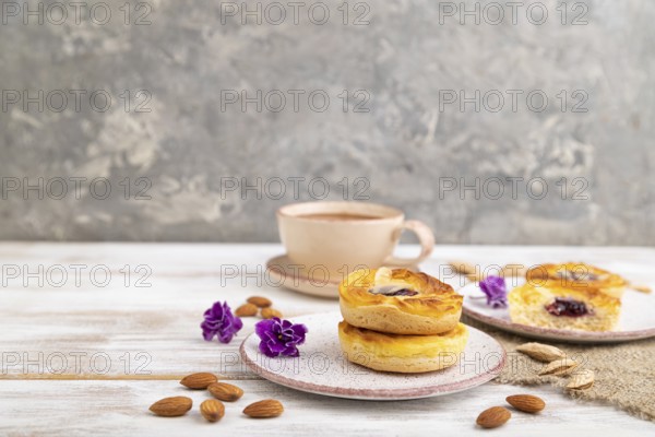 Small cheesecakes with jam and almonds with cup of coffee on a white wooden background and linen