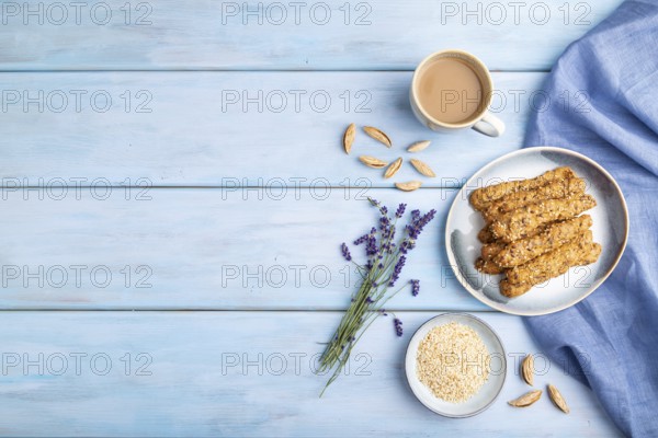 Crumble cookies with seasme and almonds on ceramic plate with cup of coffee and blue linen textile