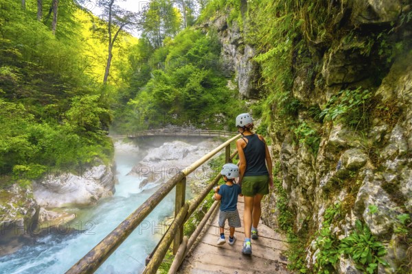 Mother and son wearing helmets walking on wooden path and enjoying breathtaking view of radovna