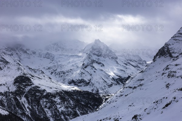 Dark clouds and wafts of mist surround the snow-covered summit of Mount Le Besso, view from the