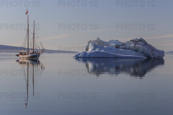 Traditional sailing ship reflected in fjord next to iceberg, sunny, Ittoqqortoormiit, Scoresby
