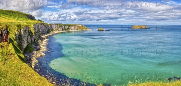 Vast coastal landscape with cliffs and bright blue sea under partly cloudy skies, County Antrim