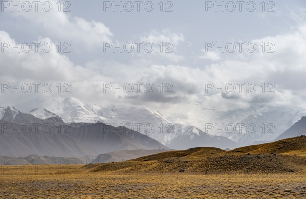 Glaciated, cloud-covered mountain peaks and golden meadows, Lenin Peak, Trans Alay Mountains, Pamir