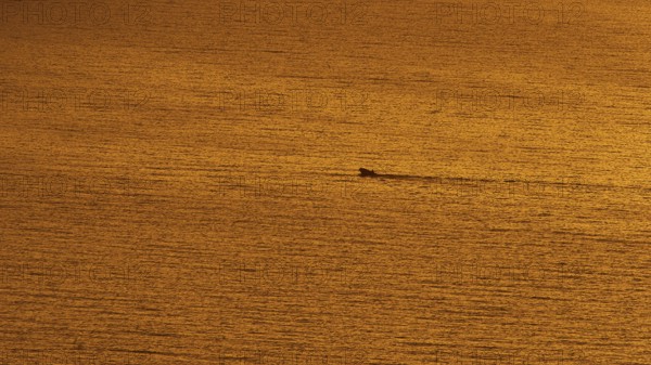 Small boat sails through the calm orange sea at sunset, Kritinia Castle, St John's Castle,