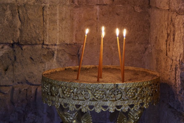 Several burning candles in an antique golden candlestick in front of a stone wall, creating a calm