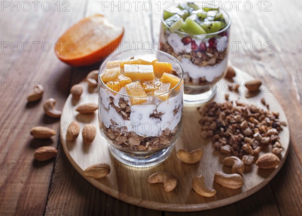 Dessert with greek yogurt, granola, almond, cashew, kiwi and persimmon on brown wooden background.