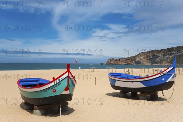 Two fishing boats on the sandy beach of Nazaré with a view of the sea and the cliffs, Praia da