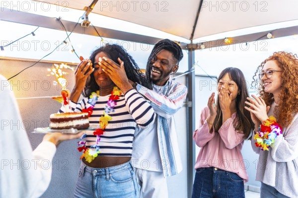 African young woman with eyes covered receiving a birthday cake from multi-ethnic friends at