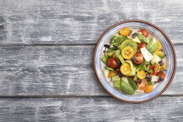 Vegetarian salad of pac choi cabbage, kiwi, tomatoes, kumquat, microgreen sprouts on gray wooden