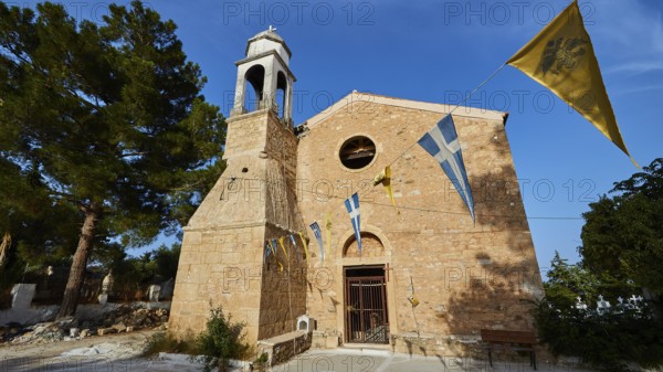 Church entrance with bell tower and Greek flags under a bright blue sky, Koroni, Byzantine