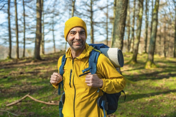 Hiker in a bright yellow jacket and backpack smiling while trekking through a sunlit forest,