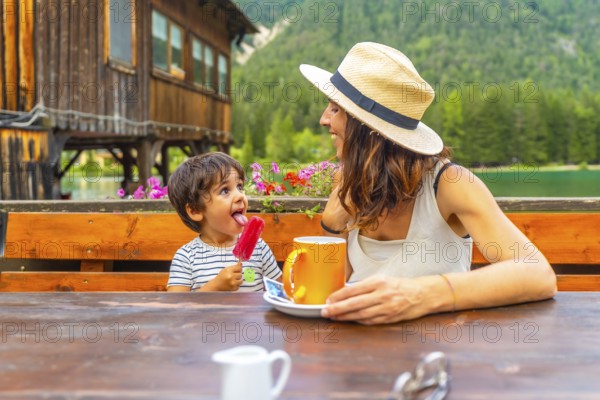 Mother and son enjoying a lakeside snack with a colorful popsicle and warm beverage against a