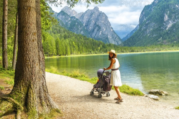 Tourist walking with stroller along lake in breathtaking mountain scenery of dolomites, italy,