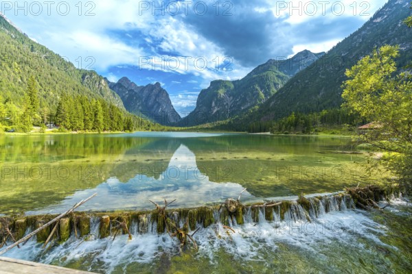 Crystal clear water flowing from lake dobbiaco, surrounded by majestic dolomites peaks, on a sunny