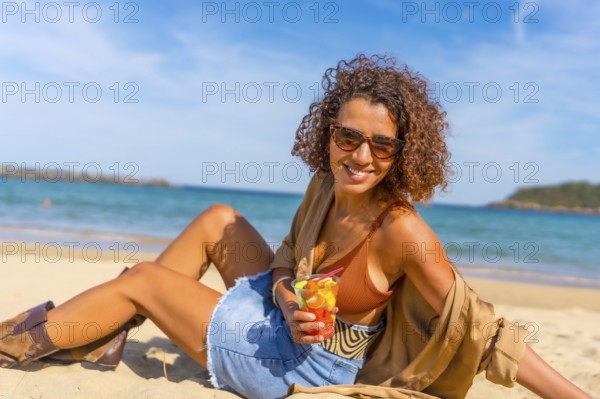 Happy sensual woman sitting on sandy beach enjoying tropical fruit sliced inside a plastic take