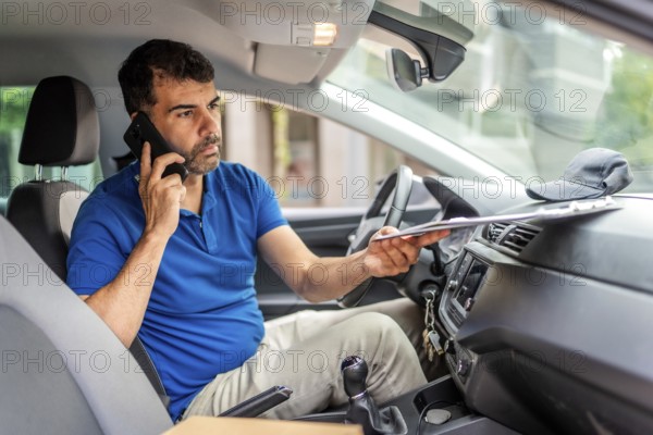 Mature caucasian male delivery person talking to the mobile phone sitting inside a van