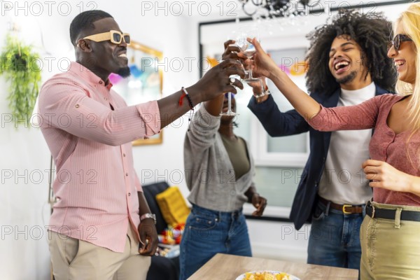Happy multi-ethnic friends toasting celebrating at home standing around a table with snacks in the
