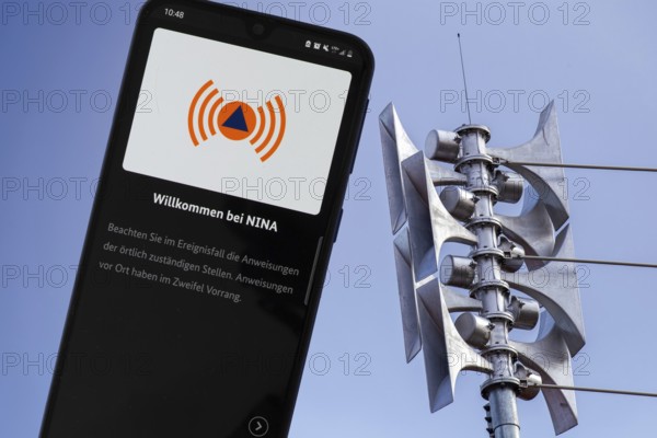 (Photomontage) Close-up of a siren at a school, next to it the open warning app NINA on a