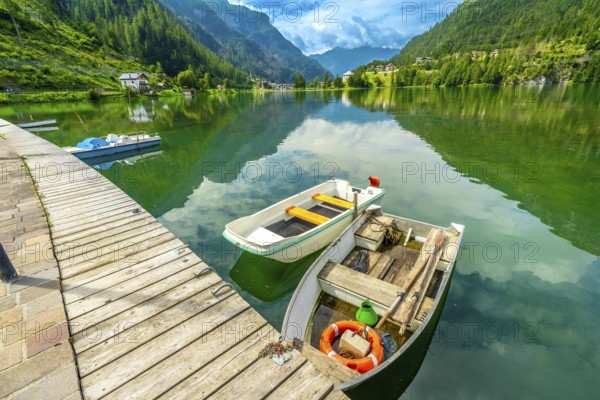 Wooden pier with boats reflecting in the emerald waters of alleghe lake with the dolomites in the
