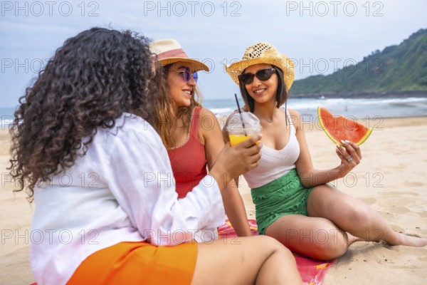 Multiethnic female friends enjoying summer on the beach on vacation, outdoors talking sitting on