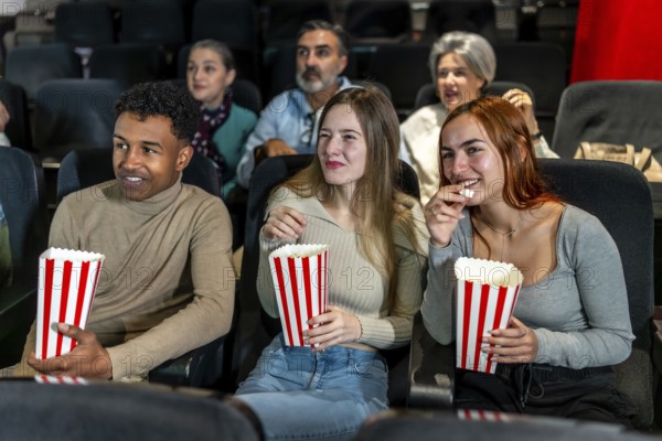 Group of friends watching a film at the movie theatre, eating popcorn and enjoying their leisure