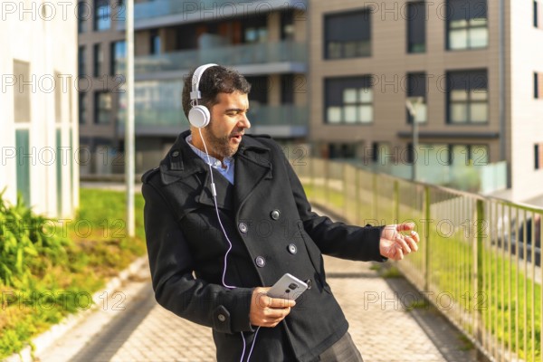Adult caucasian businessman in casual winter clothes dancing while listening to music with mobile
