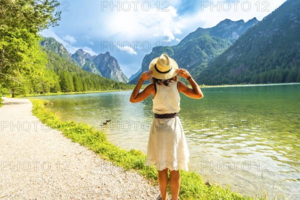 Tourist holding her straw hat admiring the stunning landscape of lake dobbiaco and the dolomites