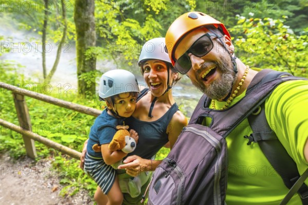 Happy family wearing helmets taking a selfie while hiking on a trail next to a river in vintgar
