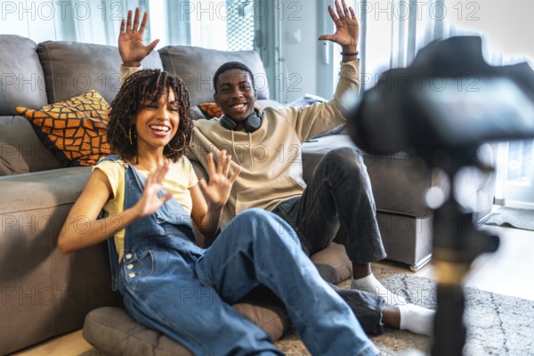 Two influencers happily waving at the camera while recording a video blog from their cozy living