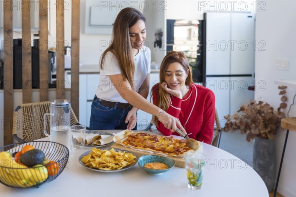 Two women enjoying a meal together, sharing pizza, tacos, nachos, and other snacks in a bright,