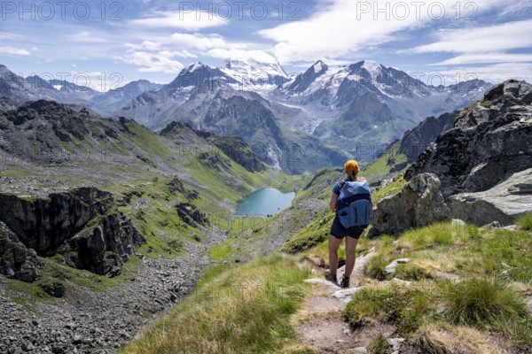 Hiker on hiking trail, mountain lake Lac de Louvie with glaciated summit of the Grand Combin, Val