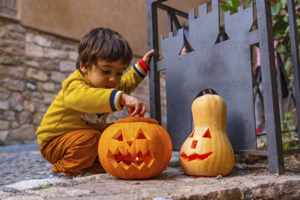 A young boy is playing with two pumpkins, one of which has a scary face. The scene is set in a