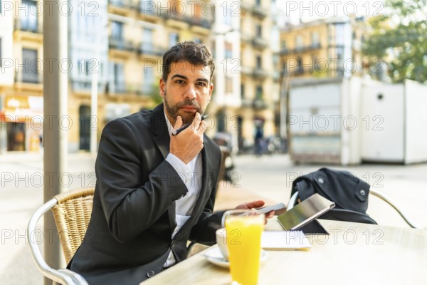Thoughtful businessman gesturing hand on chin while working using mobile phone and digital tablet
