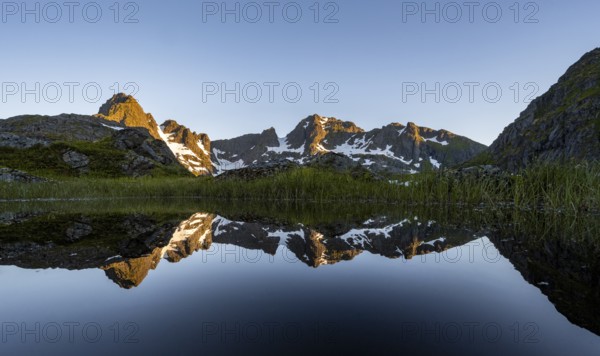 Rocky mountain peaks reflected in a small pond, mountain landscape with alpenglow at sunrise, at