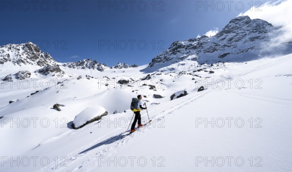 Ski tourers ascending through picturesque snow-covered mountain landscape with Piz Kesch summit,