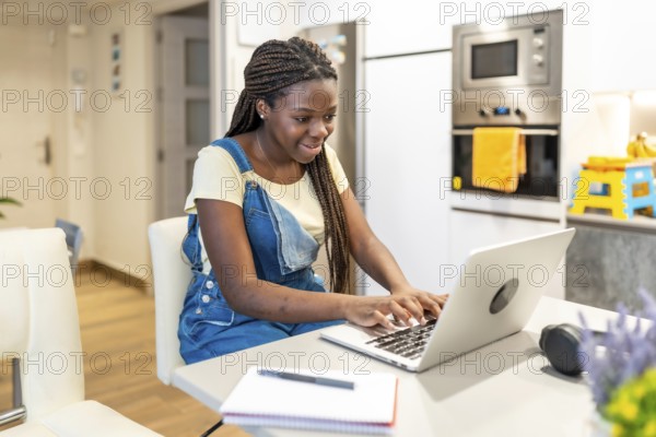 Young student concentrating on her studies, typing on a laptop in a modern kitchen, demonstrating