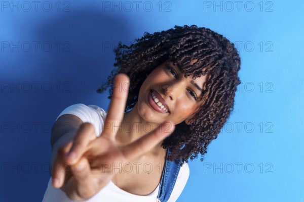 Cheerful young woman smiling and making a peace sign with both hands against a vibrant blue