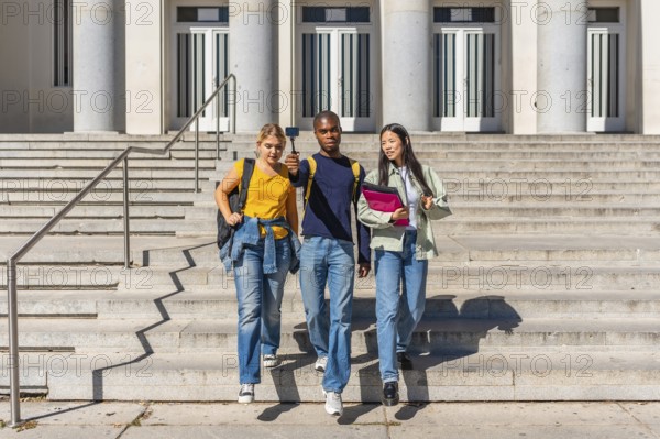 Three multi-ethnic university students walking down stairs recording online video blog with