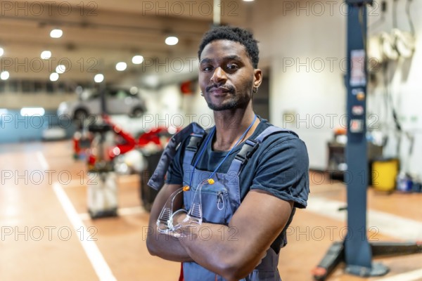 Young african american mechanic standing with crossed arms and protective eyewear in a car repair