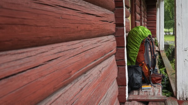 A pilgrim's rucksack standing against a wooden shed painted falun red, medieval church, pole,