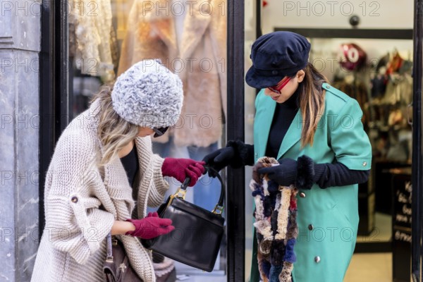 Young blonde girl shopping in the city and served by a shop assistant, looking at shop windows of